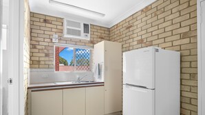 A kitchen with a brick wall, a white refrigerator, and a window with a view of a red-roofed building. - City Motor Inn Toowoomba (South Toowoomba)