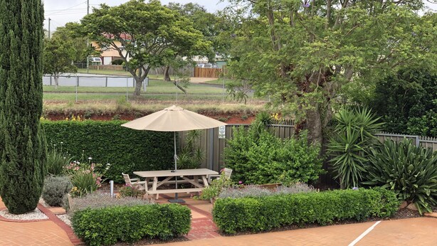 A patio area with a table and an umbrella, surrounded by well-maintained hedges and various plants. - City Motor Inn Toowoomba (South Toowoomba)