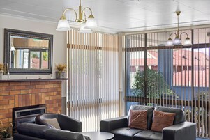 Una sala de estar moderna con chimenea, sofá de cuero y un ventanal con persianas.