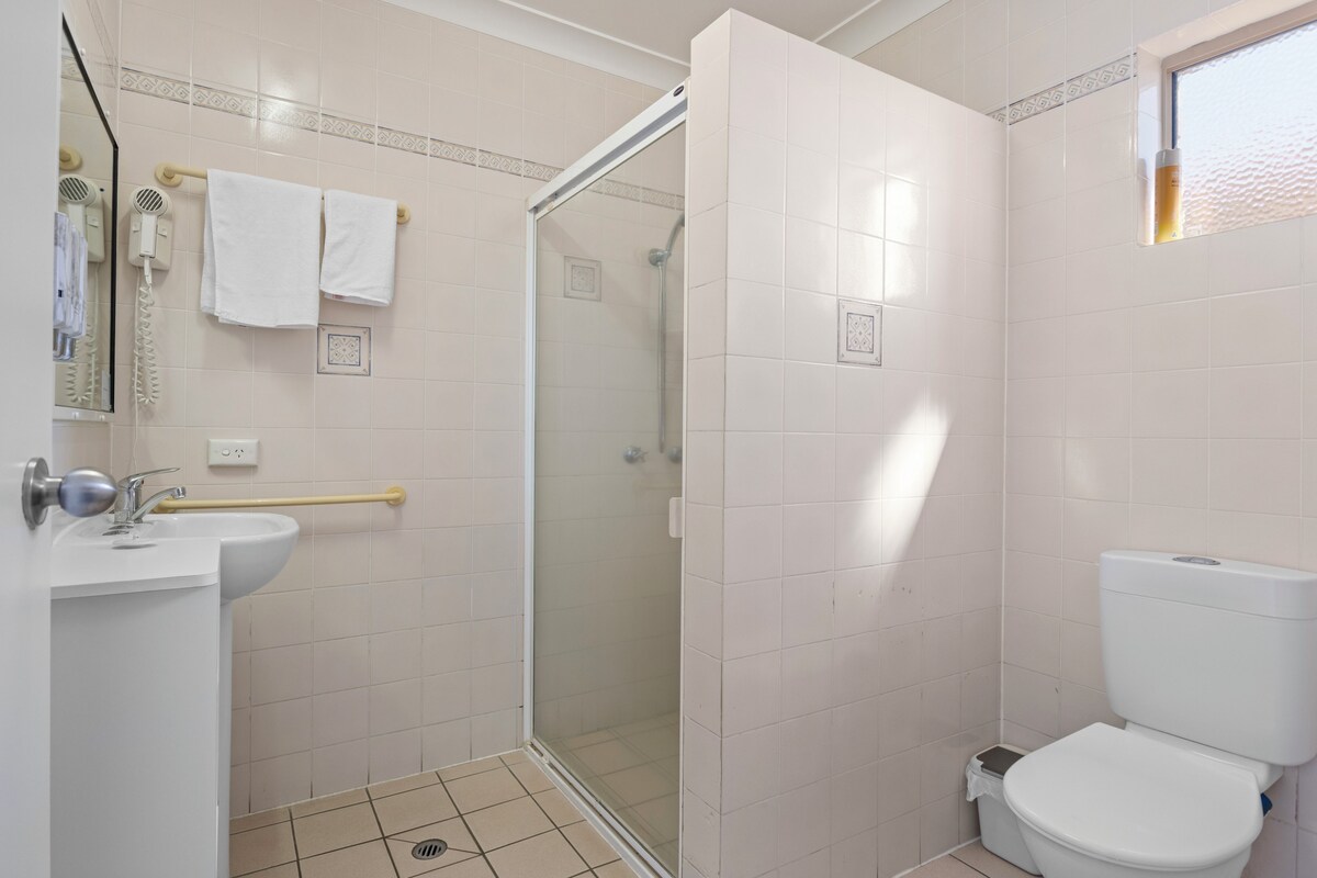 A bathroom with a shower, toilet, sink, and a towel rack.