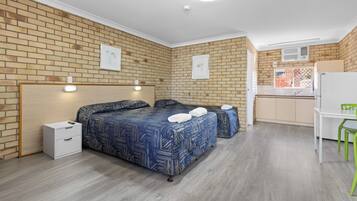 A hotel room with a brick wall, a bed with patterned bedding, a desk, a chair, and a small kitchenette.