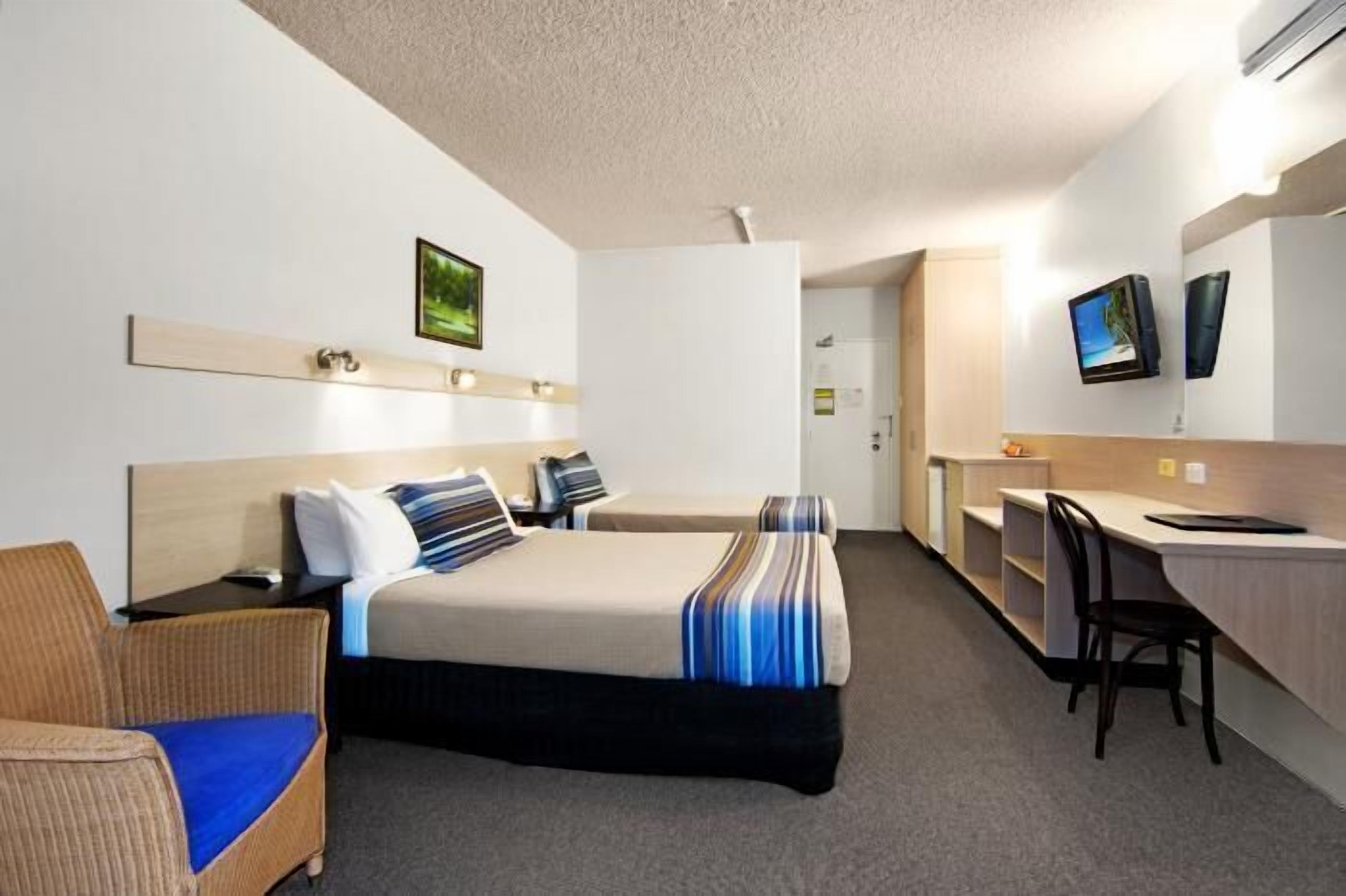 Una habitación de hotel con dos camas, un escritorio, una silla y un televisor.