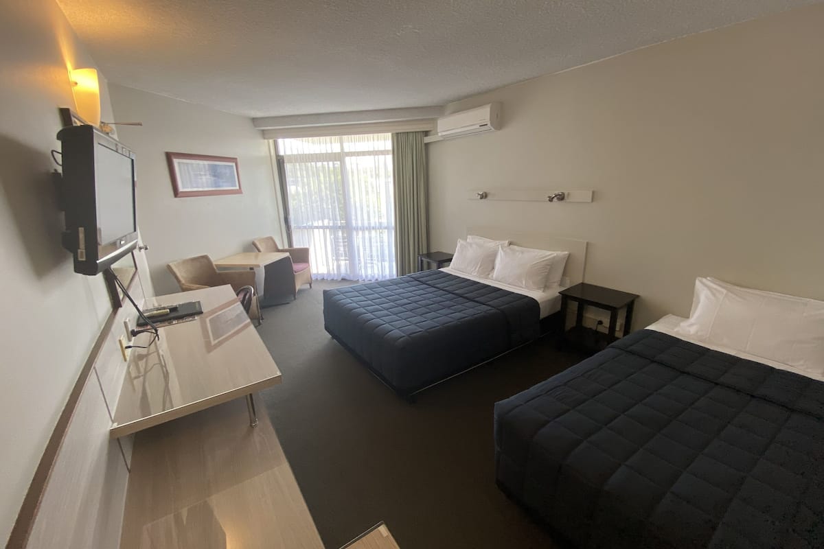 A hotel room with a desk, two beds, a TV, and a window with curtains.