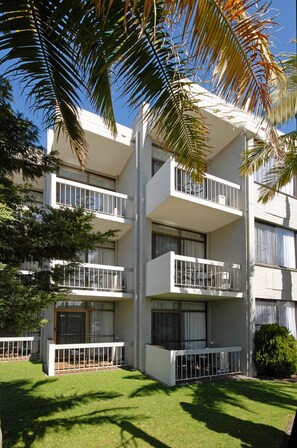 A multi-story building with balconies, a well-maintained lawn, and palm trees. - East Port Motor Inn (Port Macquarie)