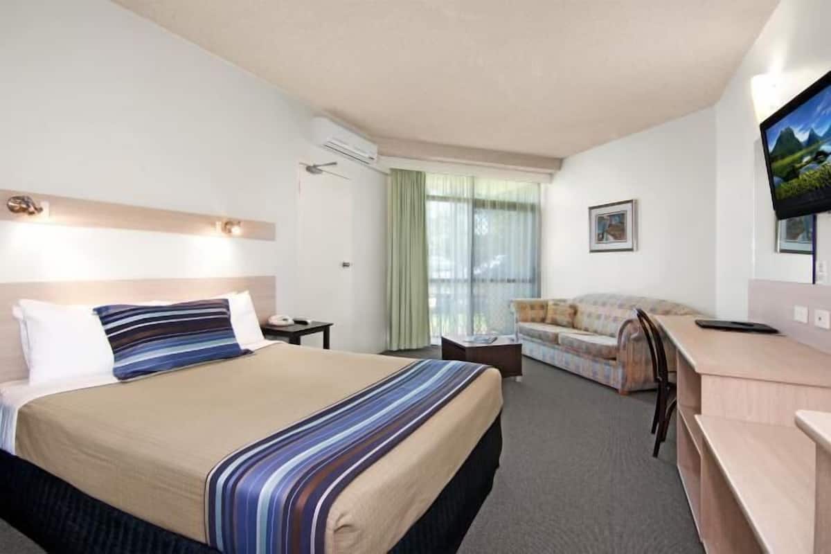 A hotel room with a bed, a desk, a sofa, a TV, and a window with curtains.