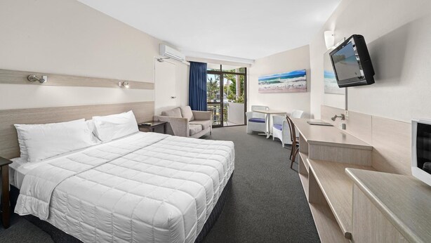 A hotel room with a large bed, a desk, a chair, a TV, and a window with a view of the outdoors. - East Port Motor Inn (Port Macquarie)