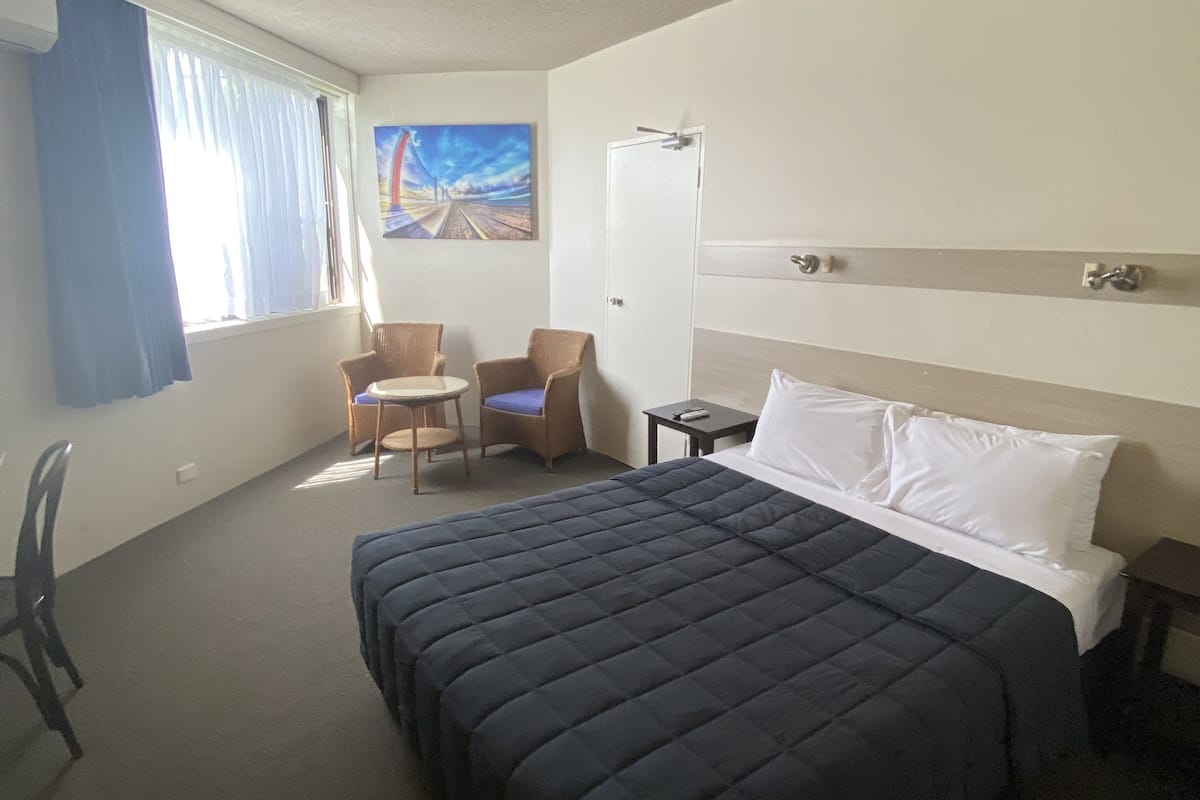 A hotel room with a large bed, a desk, a chair, and a painting on the wall.