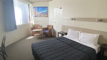 Ett hotellrum med en stor säng, ett skrivbord, en stol och en tavla på väggen.