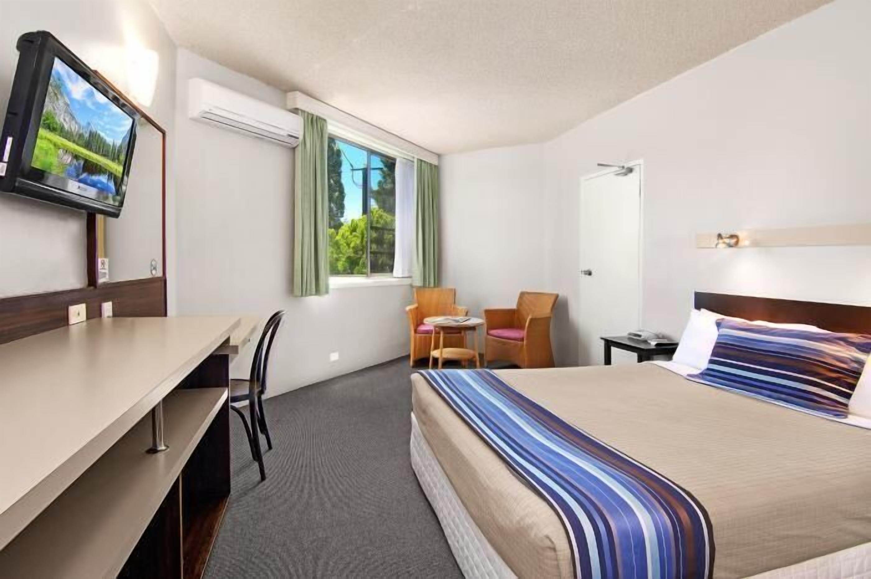 A hotel room with a bed, a desk, a chair, a television, and a window with curtains.