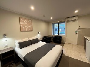 A hotel room with a bed, a desk, a chair, a window with a view, and an air conditioning unit. - Ryley Motor Inn (Wangaratta)