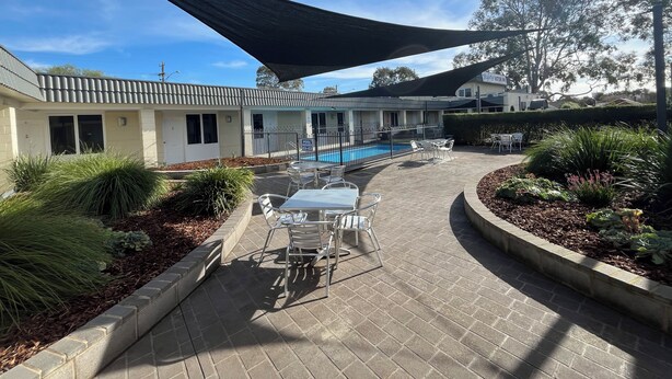 A pool area with a shaded patio, outdoor seating, and a building with a tiled roof. - Ryley Motor Inn (Wangaratta)
