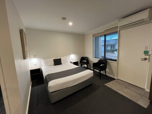A hotel room with a bed, two chairs, a window, and a door.