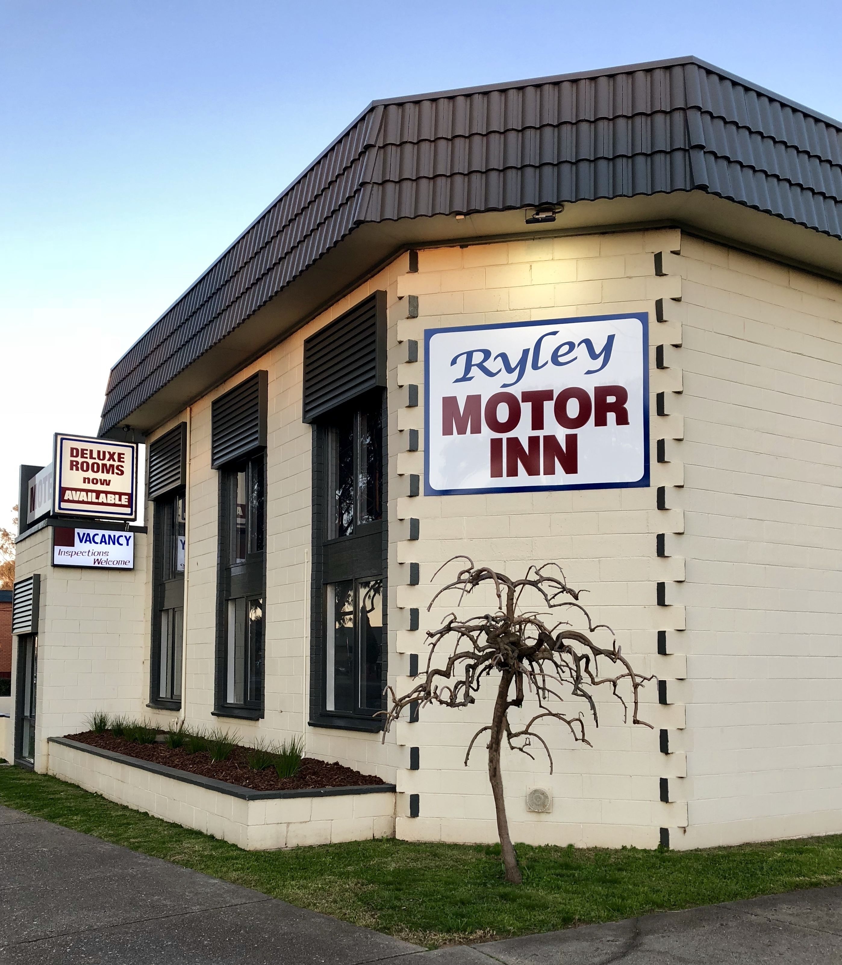 Un edificio con un'insegna che riporta "Ryley Motor Inn" e un'altra che indica "Camere Deluxe Disponibili Ora".