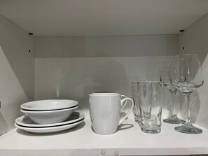 Une étagère blanche sur laquelle sont empilées des bols blancs, une tasse blanche et des verres à vin transparents.