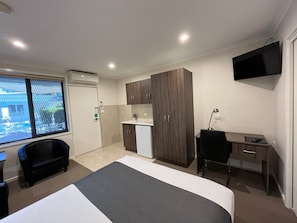 Habitació d'hotel amb llit, escriptori, cadira, petita cuina i televisió.