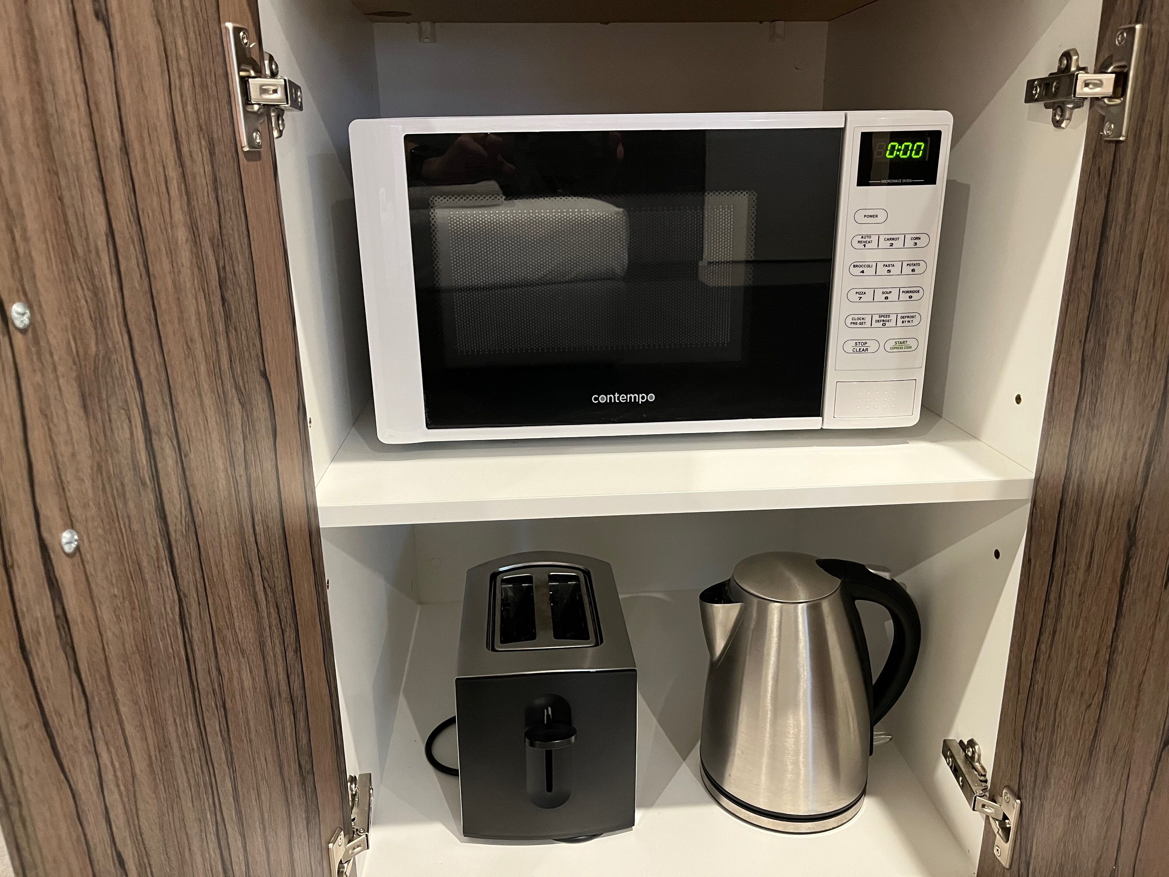 A microwave on a white shelf, a toaster, and a kettle in a wooden cabinet.