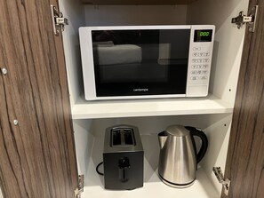 A microwave on a white shelf, a toaster, and a kettle in a wooden cabinet.