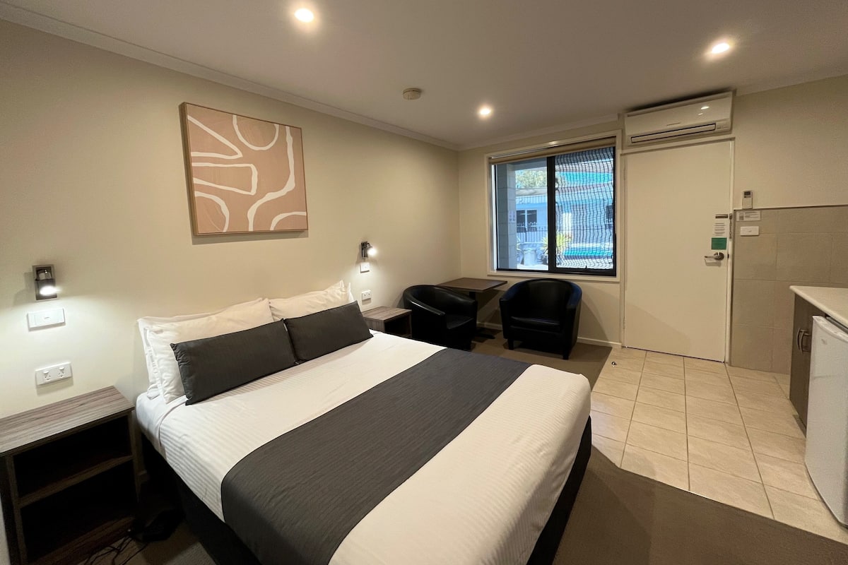 Quarto de hotel com cama, escrivaninha, cadeira, janela com vista e ar condicionado.