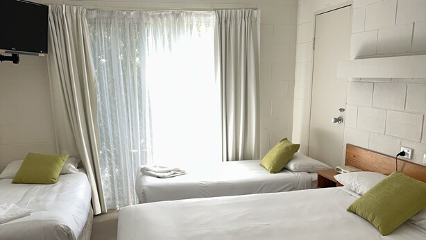 Une chambre d’hôtel avec deux lits, un ventilateur de plafond, une télévision et une fenêtre avec des rideaux.