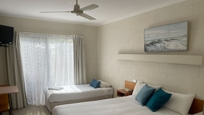 Une chambre d’hôtel avec deux lits, un ventilateur de plafond, un tableau au mur et une fenêtre avec des rideaux.