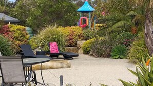 Un jardín con mobiliario exterior, un parque infantil y diversas plantas.