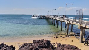 Un muelle se adentra en un mar azul y transparente con un barco amarrado al final.