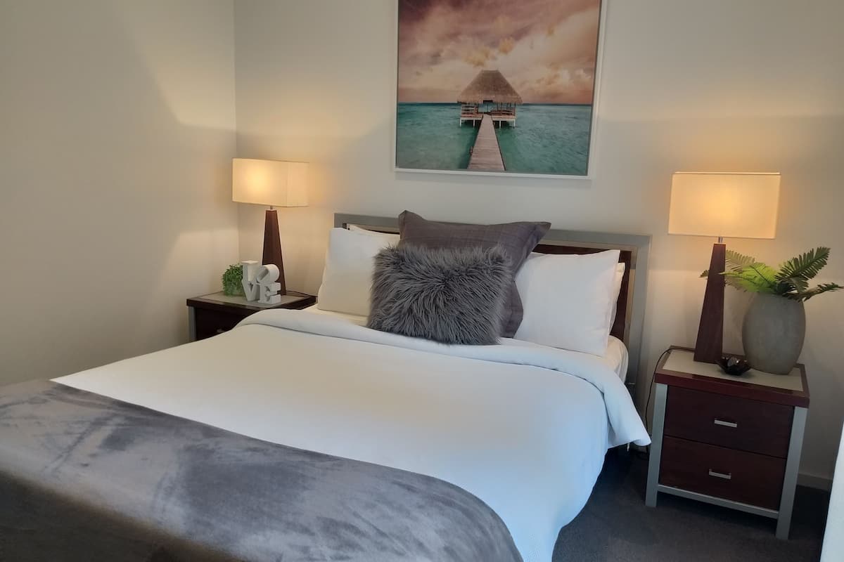 A neatly made bed with a fluffy pillow, two bedside tables with lamps, a small decorative item, and a framed picture of a boat on a pier.