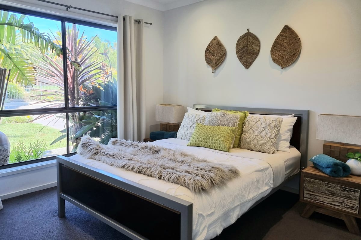 A bedroom with a large bed, a view of greenery outside, and three wall-mounted decorative leaves.