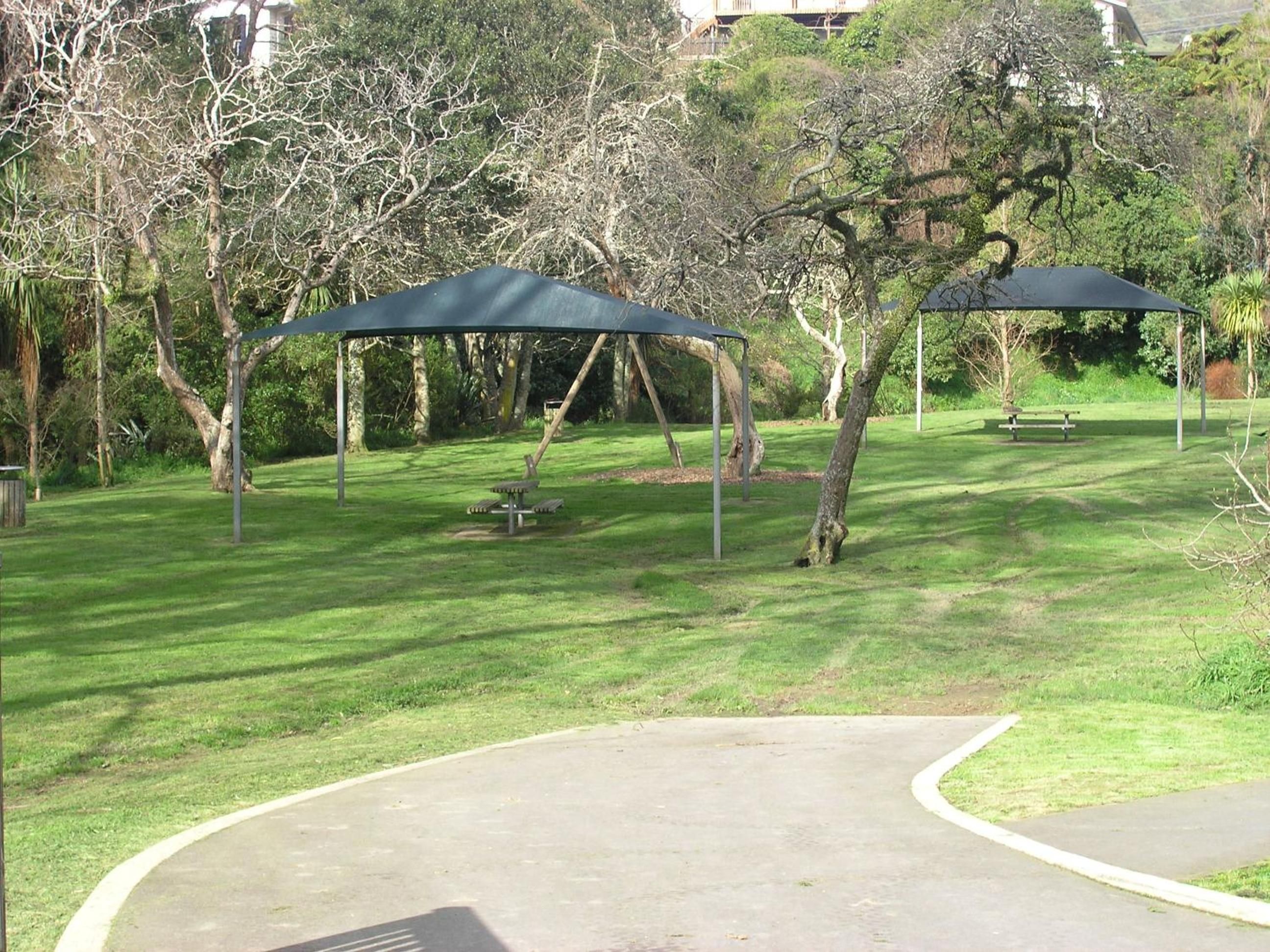 A park with a paved walkway, picnic tables, and a covered seating area.