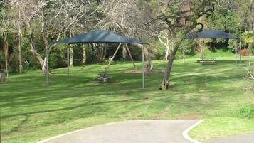 A park with a paved walkway, picnic tables, and a covered seating area.