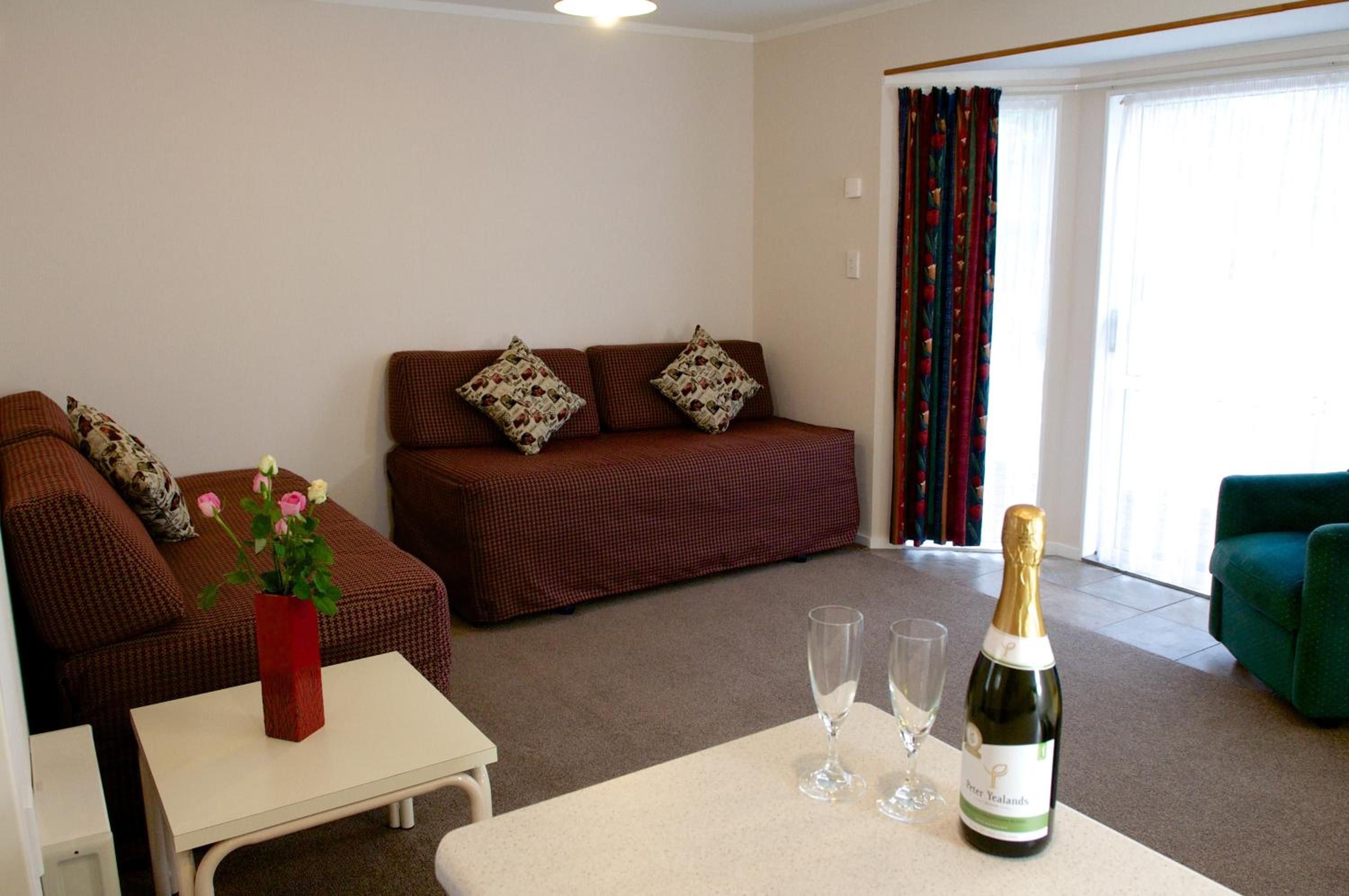 A living room with a sofa, a small table with a vase of flowers, and a bottle of champagne.