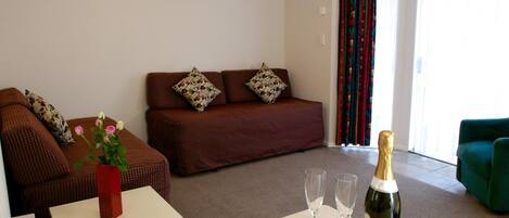 A living room with a sofa, a small table with a vase of flowers, and a bottle of champagne.
