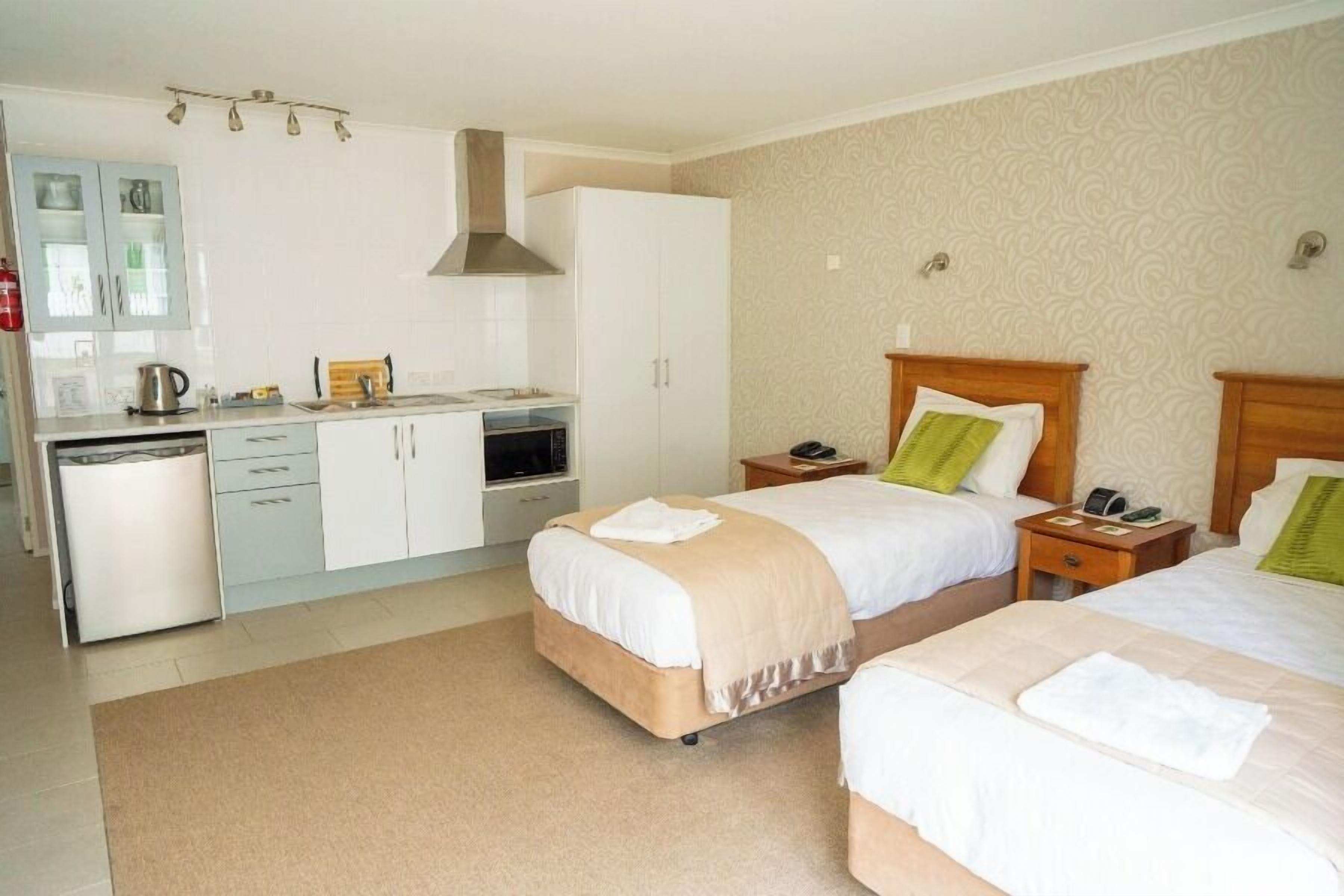 A hotel room with two beds, a kitchenette, and a bathroom.