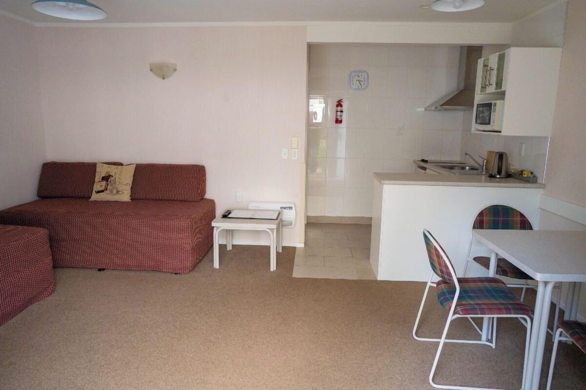 A compact living space with a sofa, a small table, a kitchenette, and a dining area with chairs.