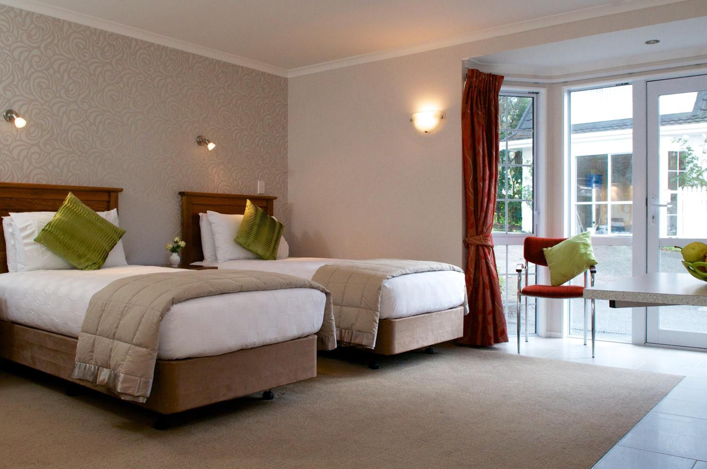 A hotel room with two beds, a small table, a chair, and a view of the outdoors.