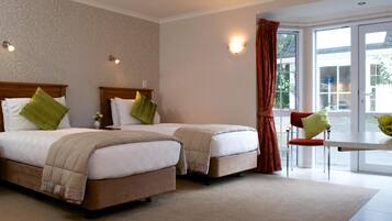 A hotel room with two beds, a small table, a chair, and a view of the outdoors.