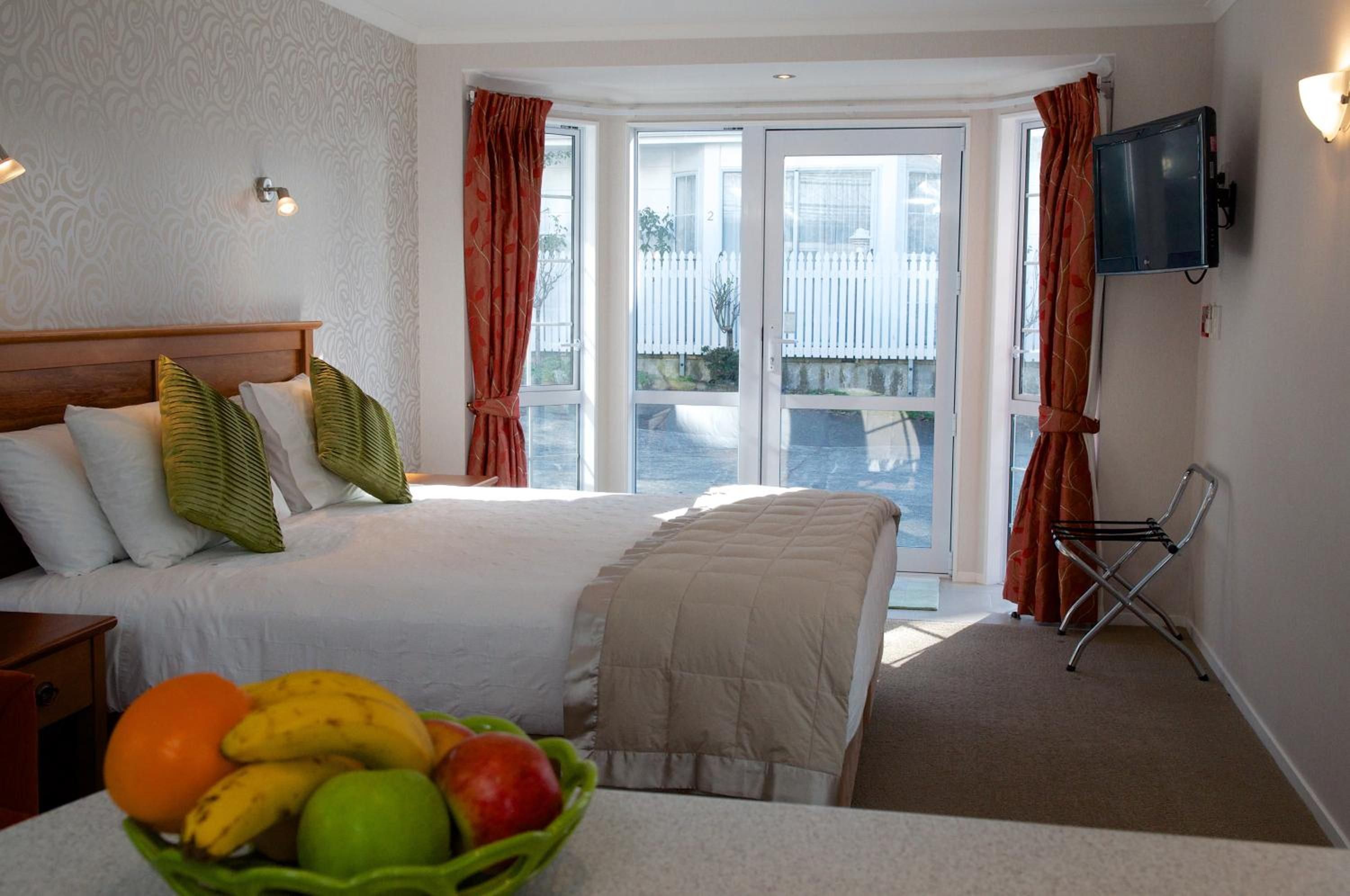 A hotel room with a bed, a television, a window with curtains, and a fruit bowl on the table.