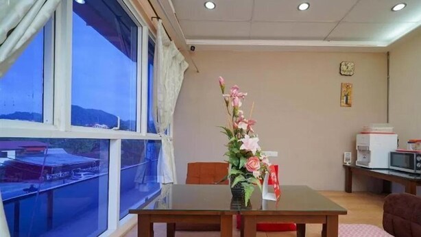 A room with a large window, a wooden table, a vase with flowers, a microwave, and a clock on the wall. - Hotel O V Stay Guesthouse (George Town)