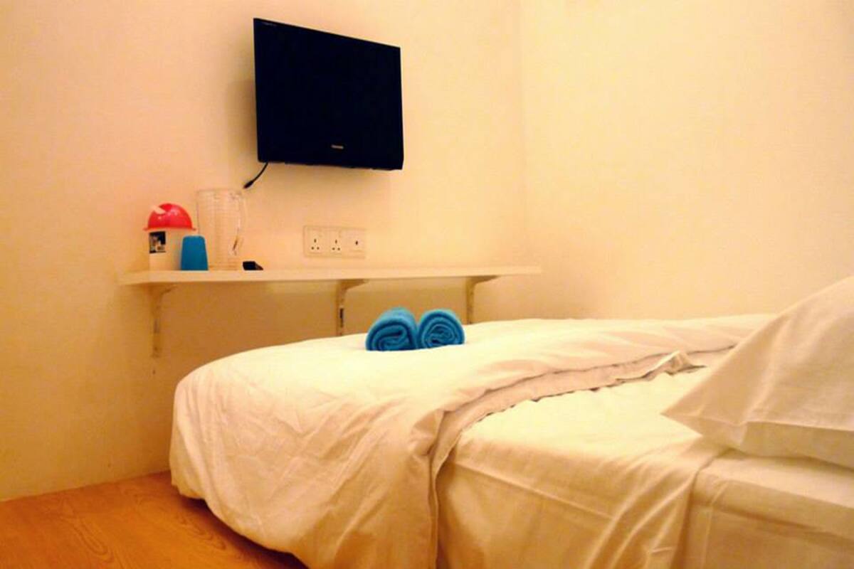 A hotel room with a bed, a mounted TV, a shelf with toiletries, and a power outlet.
