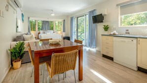 Una cocina moderna con lavavajillas, un comedor con mesa de madera y sillas de mimbre, y una sala de estar con sofá y televisor.