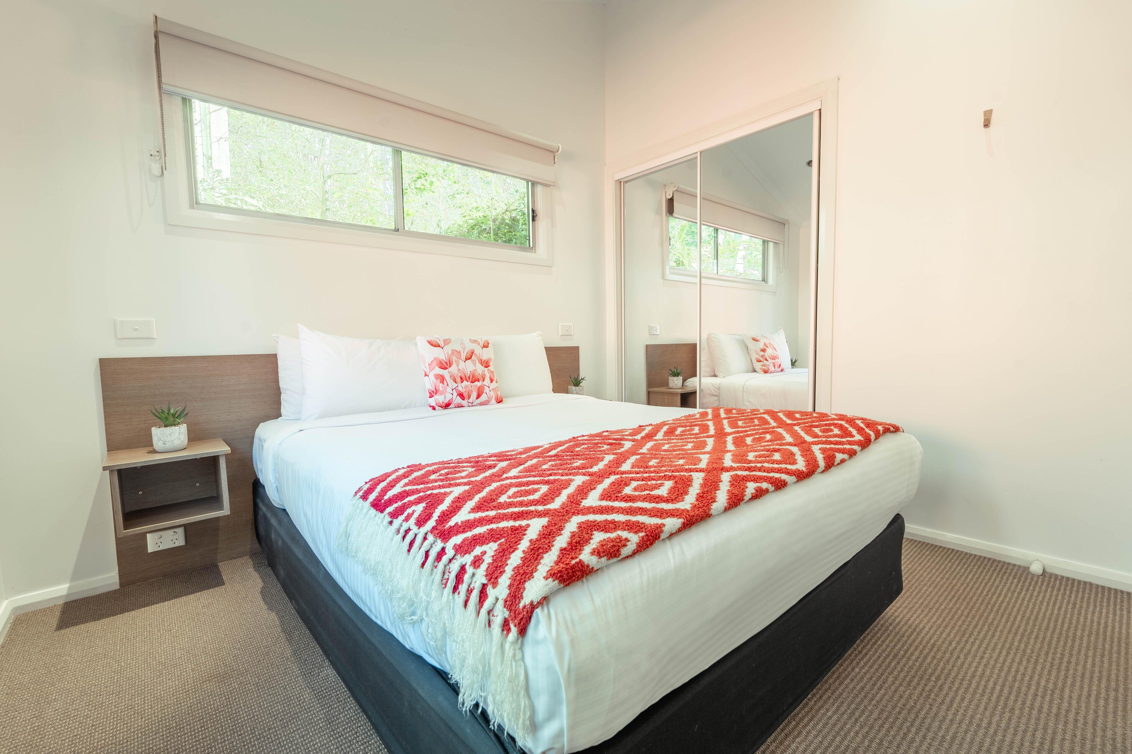 A bedroom with a bed, a nightstand, a mirror, and a window.