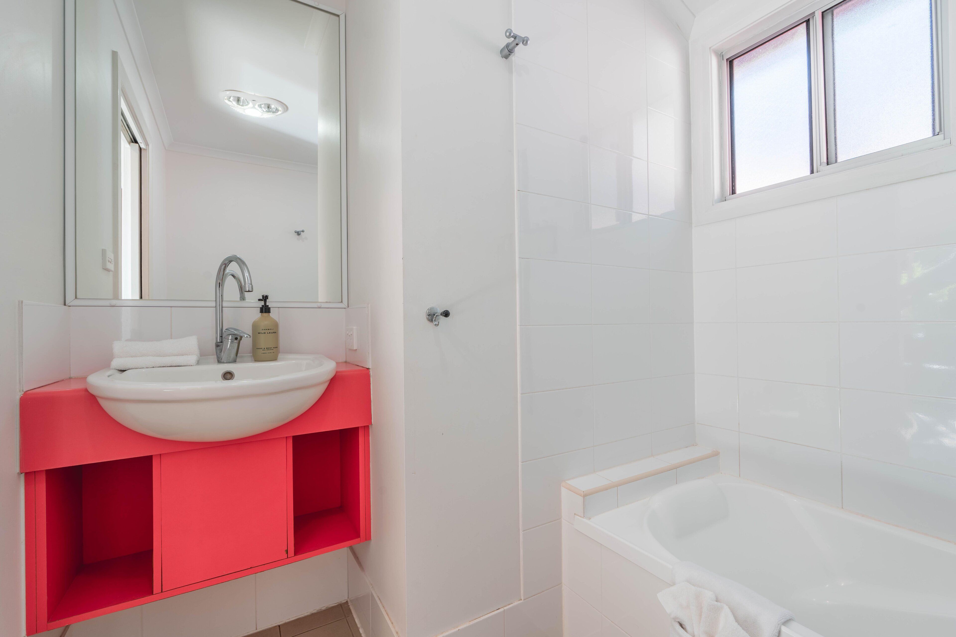 Un baño moderno con lavamanos blanco, tocador rojo, un espejo grande, ducha y bañera.