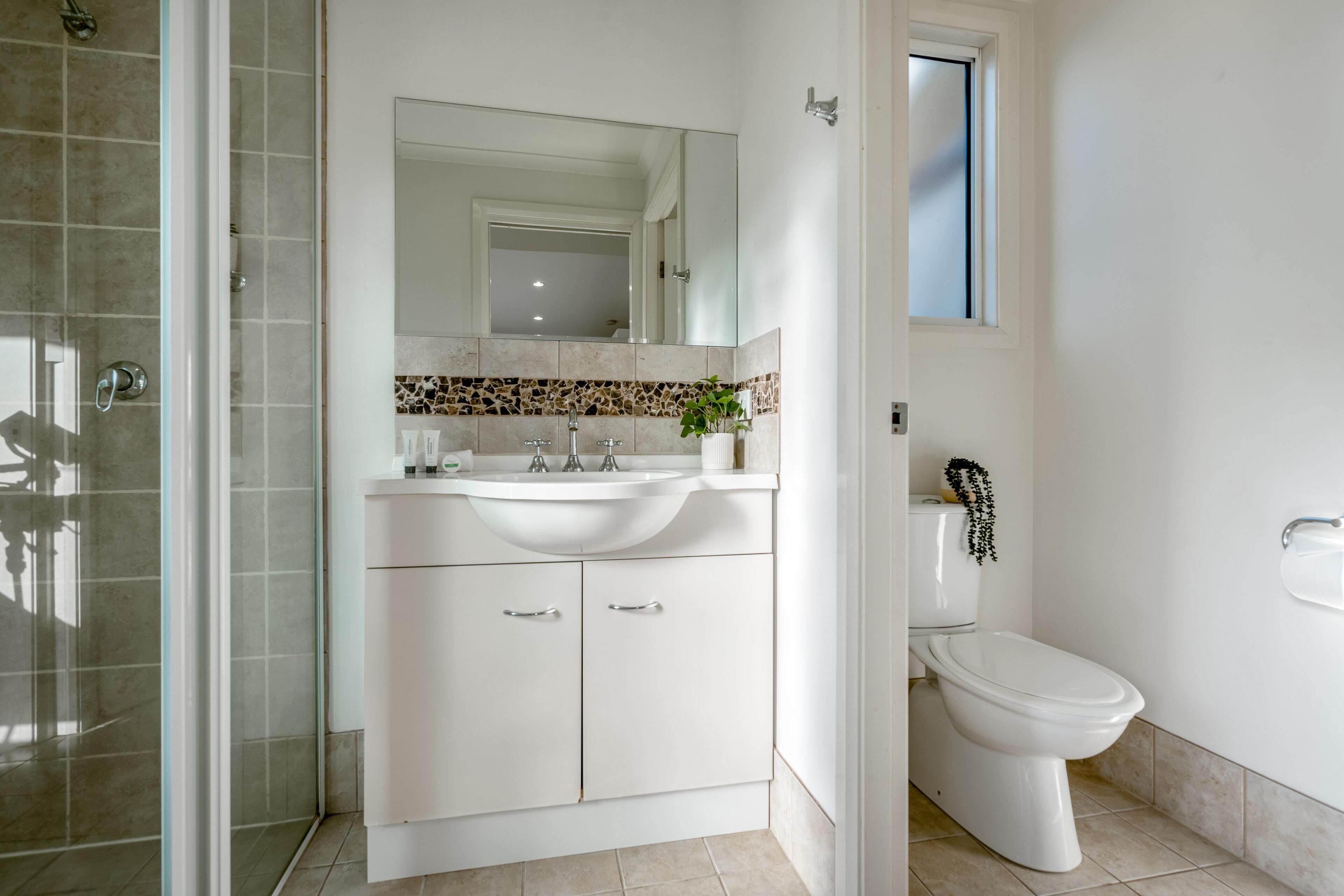 A modern bathroom with a glass shower enclosure, a white sink with a mirror above it, and a toilet.