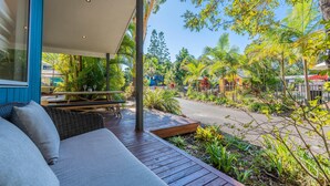 Un espacio al aire libre con techo, que cuenta con una terraza de madera, un sofá y una mesa con sillas.