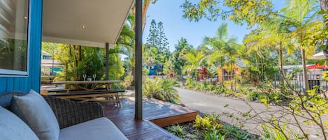A covered outdoor seating area with a wooden deck, a sofa, and a table with chairs.