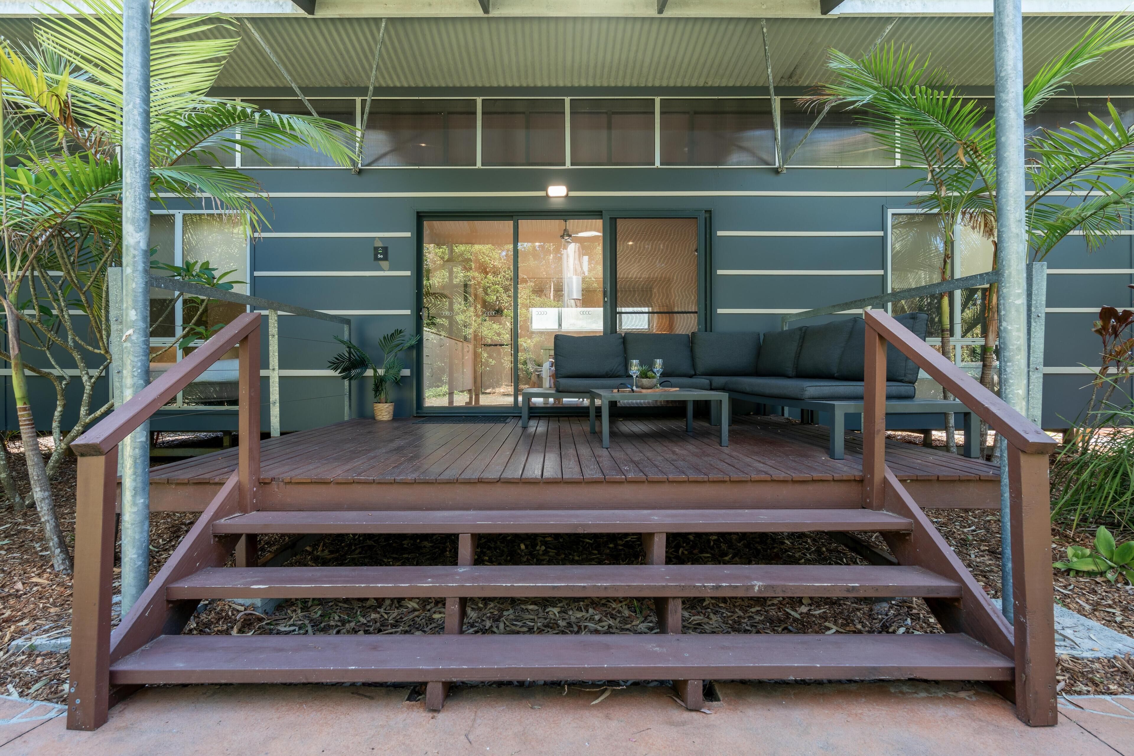 A modern outdoor deck with a wooden staircase leading to a seating area with a sofa and coffee table.