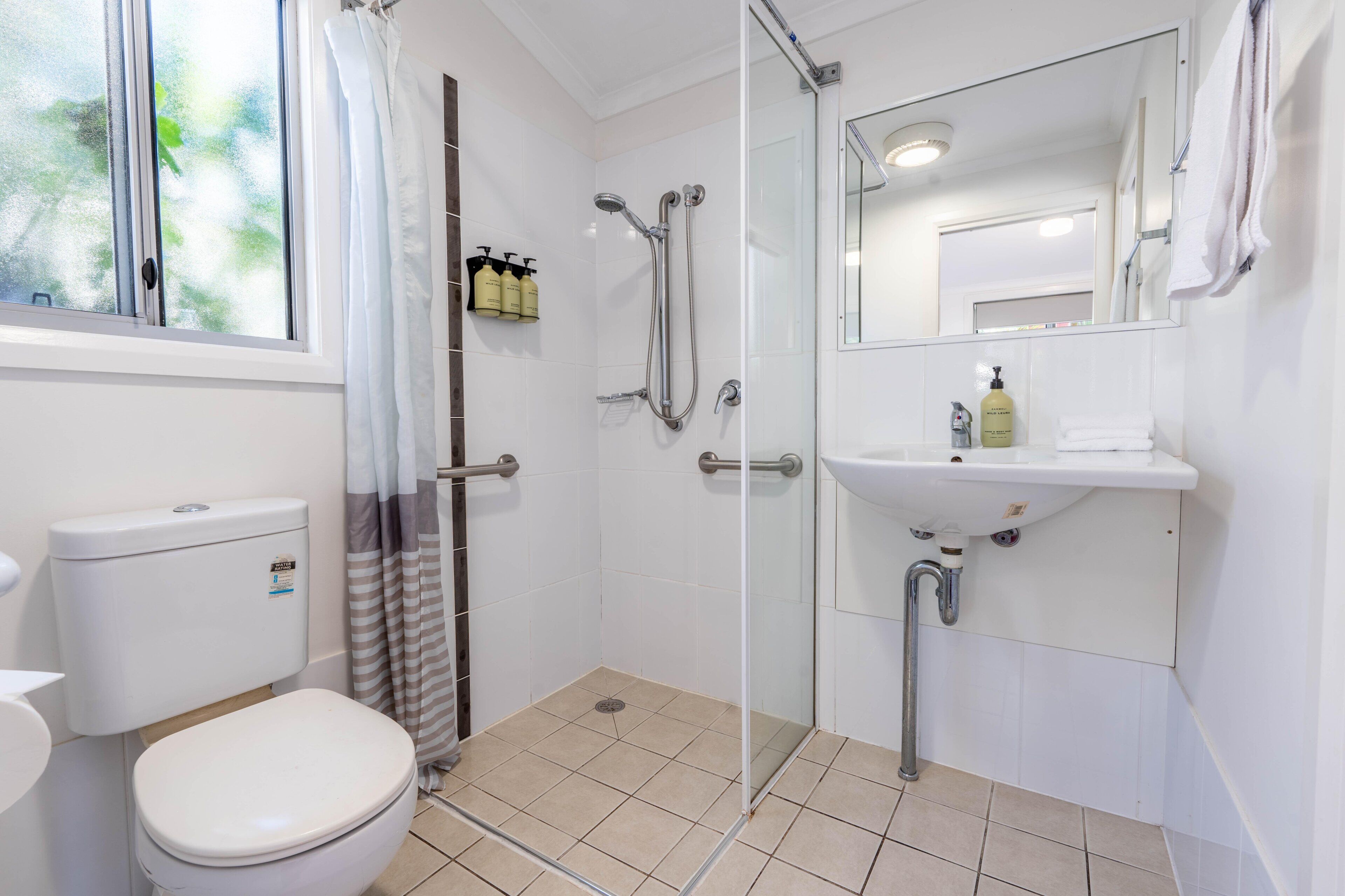 A bathroom with a toilet, shower, sink, and mirror.