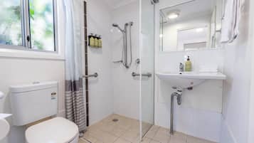 A bathroom with a toilet, shower, sink, and mirror.
