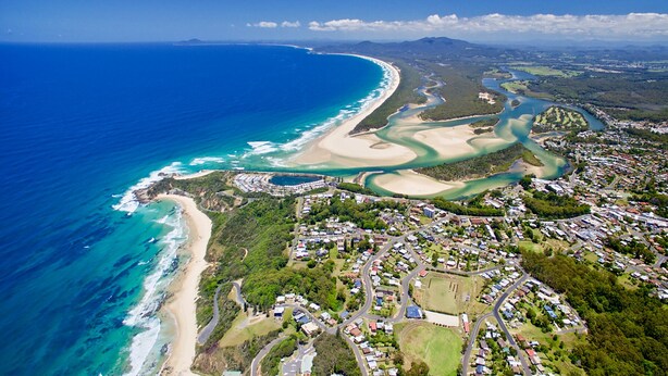 Vista aérea de un pueblo costero con playa, carreteras y zonas residenciales.