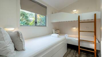 A bedroom with a bunk bed, a window with a view of greenery, a wooden ladder, and a bedside lamp.